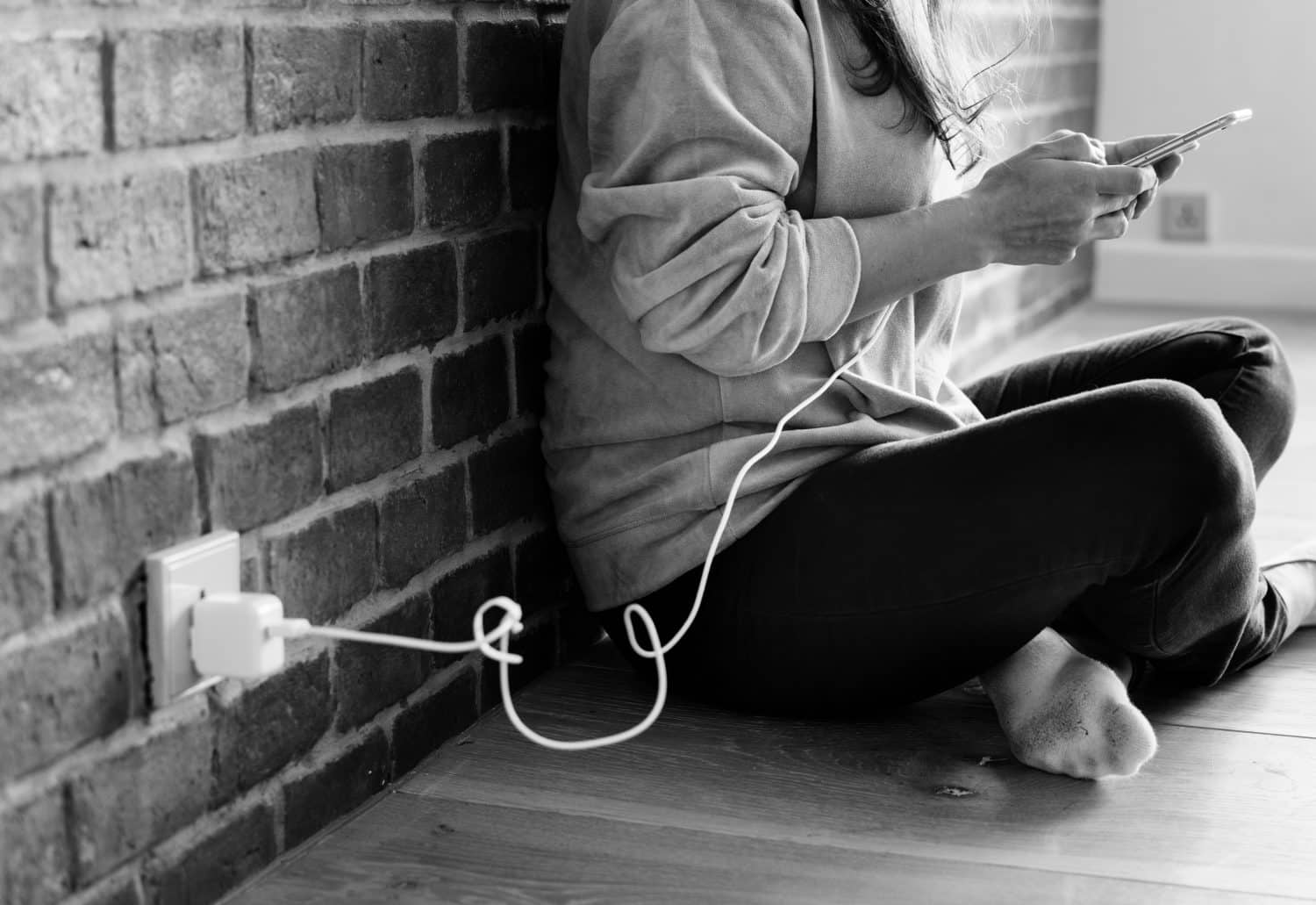 grayscale photo of person sitting beside wall using smartphone