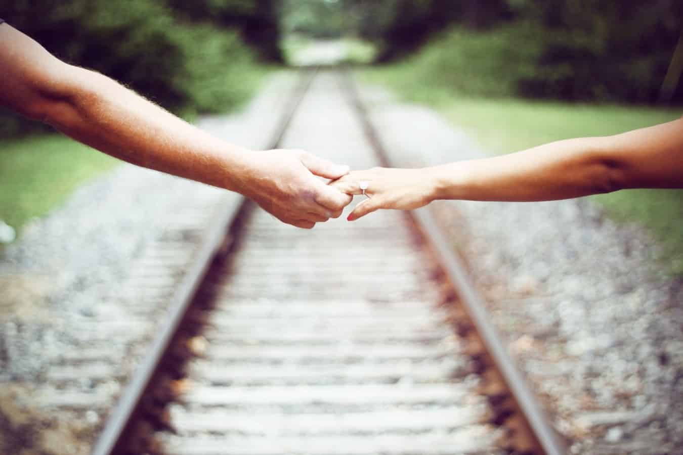 Two people hold hands near a railway station.