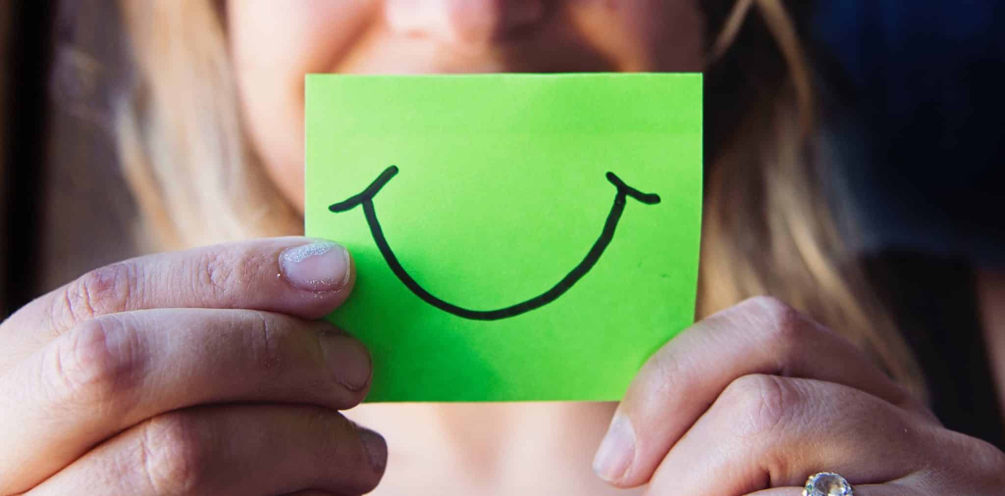 A woman holds a note in her hands that show a smiling face.